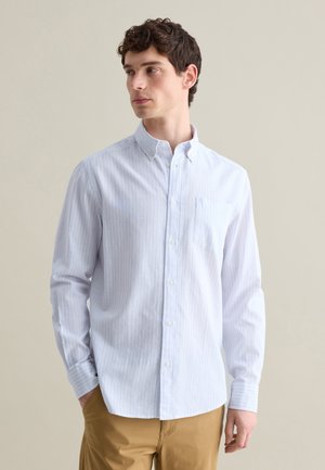 Camisa de botones a rayas en azul claro y blanco, con un bolsillo en el pecho, cuello con solapa y mangas largas, hecha de un tejido suave.