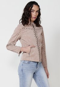 Geacă din piele bej cu un design ajustat, presărată cu prețioase metalice pe umeri și mâneci, având un fermoar central și buzunare cu fermoar.