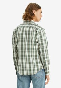 Camicia a maniche lunghe da uomo in motivo plaid verde e bianco, con polsini a bottone e orlo curvo, realizzata in tessuto di cotone intrecciato.