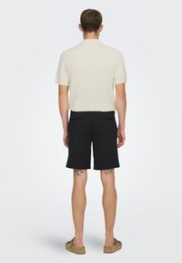 Herre kortærmet creme polo-shirt og sorte shorts. Shortsene har to baglommer med knapper, og poloen har en ribbet tekstur.