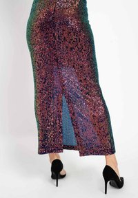 Lange, mit Pailletten verzierte Rock mit einer enganliegenden Silhouette, mehrfarbigem Design und seitlichem Schlitz. Kombiniert mit schwarzen High Heels.
