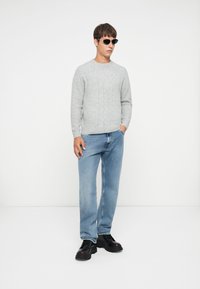 Gray knitted sweater with a cable pattern, blue straight-leg jeans, black chunky shoes, and black sunglasses. Plain white background.