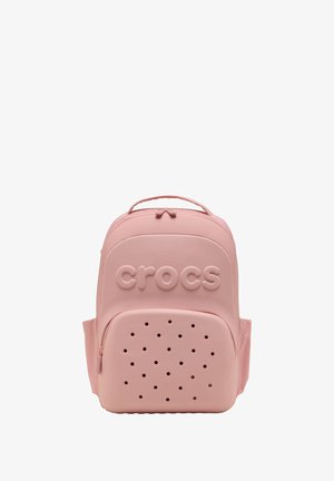 Sac à dos Crocs rose clair avec poche avant zippée, présentant des trous de ventilation et un logo Crocs en relief sur le compartiment principal.