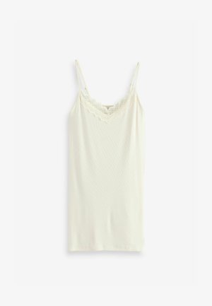 Balta kamzola, kas izgatavota no mīksta auduma ar plānām regulējamām siksnām un mežģīņu apdari gar kakla līniju, ar pieguļošu dizainu un taisnu apakšmalu.