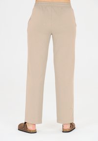 Beige, locker sitzende Sweatpants mit elastischem Bund, Seitentaschen und glatter Textur, kombiniert mit braunen Slippern.