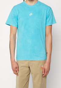 Tyrkysové bavlněné tričko s kulatým výstřihem, krátkými rukávy a bílým logem Nike na hrudi. Hladká textura, volný střih.