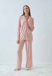 Ljusrosa satinpyjamas med en knapp-up skjorta med krage och långa ärmar, tillsammans med löst sittande byxor och kontrasterande kanter.