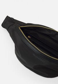 Svart midjeväska i nylon med guldglidkedja. Har en innerficka med elegant läderkant och präglad logotyp. Kompakt och funktionell design.