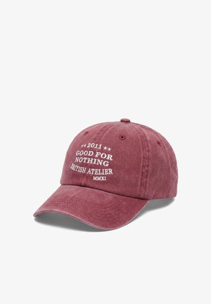 Versleten rode baseballpet met witte tekst ""2011 Good For Nothing British Atelier MMXI"" op het voorpaneel.