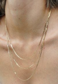 Goldfarbene mehrlagige Halskette mit drei Ketten unterschiedlicher Längen. Jede Kette hat eine glatte Oberfläche und einen dezenten Glanz.