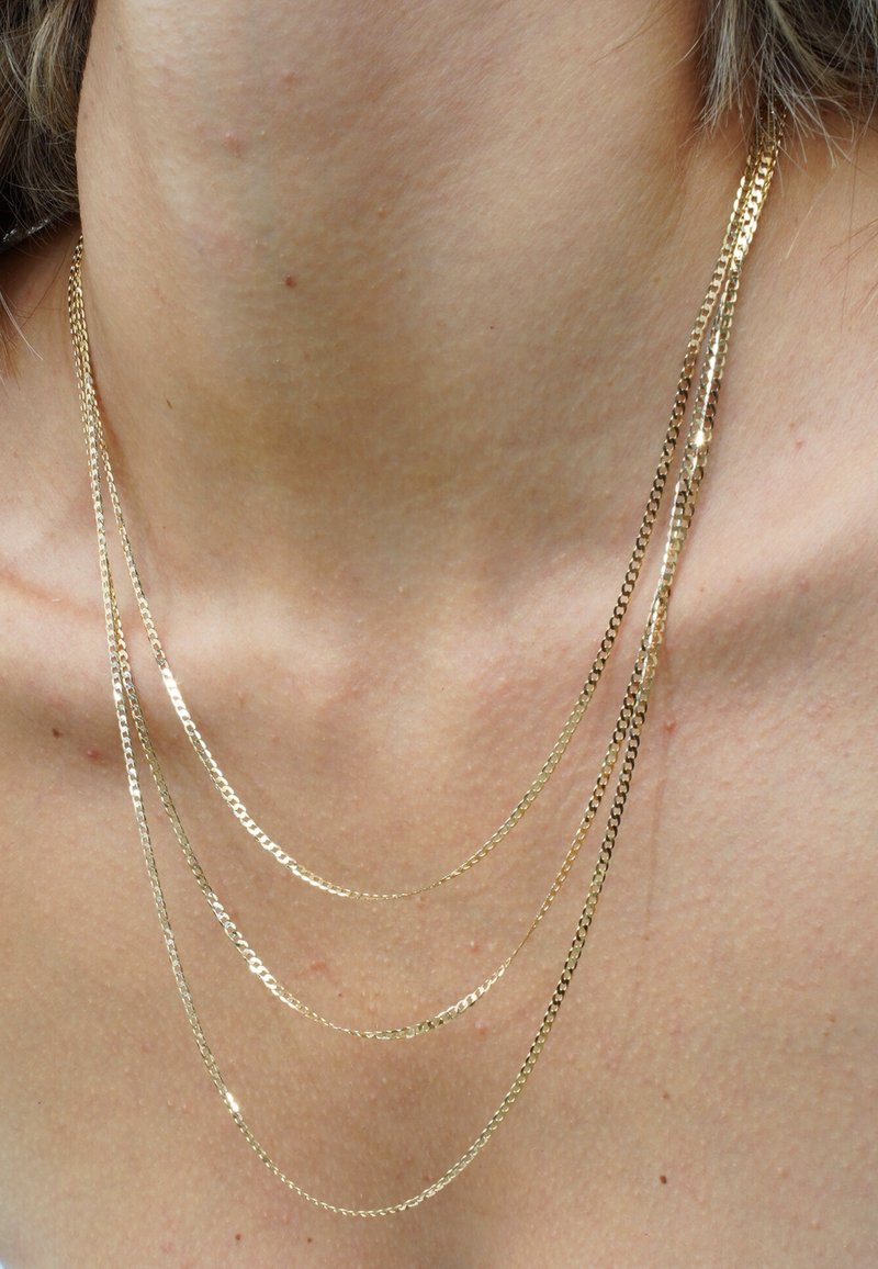 Goldfarbene mehrlagige Halskette mit drei Ketten unterschiedlicher Längen. Jede Kette hat eine glatte Oberfläche und einen dezenten Glanz.