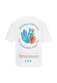 Witte t-shirt met een blauw en oranje abstract koraalontwerp, tekst "Dromen maken op een zomerse bries," en drie kleine blauwe zeepaardjes iconen eronder.
