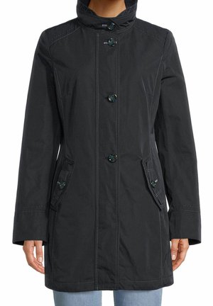 Manteau noir mi-long avec cinq boutons sur le devant, deux poches à rabat avec boutons, porté sur un jean bleu clair.