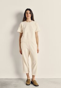 Lichtbeige fleece top en bijpassende cropped broek met een zachte textuur. Model draagt bruine instapschoenen. Eenvoudig ontwerp, rechte pasvorm.