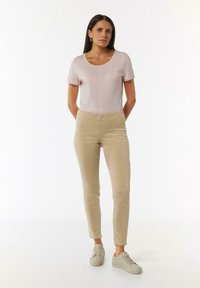 Helles rosa Oberteil mit kurzen Ärmeln und runder Ausschnitt, kombiniert mit beigefarbenen Slim-Fit-Hosen und beigen Sneakers. Einfaches, figurnahes Design ohne Muster.