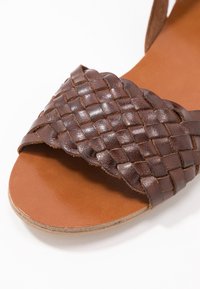 Sandale en cuir marron avec une bride tressée sur une semelle intérieure beige lisse et un design à bout ouvert.