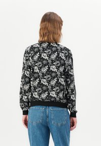Sweatshirt noir à motifs floraux blancs, avec des poignets et un ourlet côtelés, associé à un jean taille haute bleu clair, vu de dos.