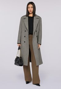 Szary wełniany płaszcz o podwójnym zapięciu, z czarnymi guzikami i szerokimi klapami; w zestawieniu z czarną bluzką i brązowymi spodniami o szerokich nogawkach, trzymając czarną torbę.