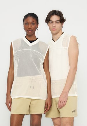 Dwie modelki stoją obok siebie ubrane w białe, bezrękawnikowe siateczkowe topy na czarnych koszulkach oraz beżowe szorty na jednolitym białym tle.