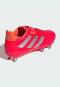 Botas de fútbol rojas y naranjas con rayas plateadas, que presentan un diseño elegante, parte superior texturizada y tacos metálicos para tracción.
