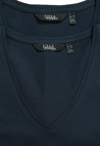 Deux tops en V bleu marine foncé en tissu doux, présentant des étiquettes pour la marque Ulla Popken au niveau du cou, indiquant 'fabriqué au Bangladesh'.