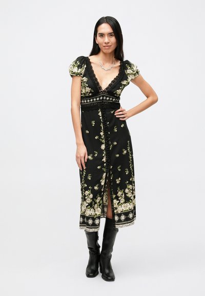 Zwarte bloemenjurk met korte pofmouwen, diepe V-hals, verfijnde kanten afwerking en een split tot op de knie, met groene en beige bloemenpatronen.