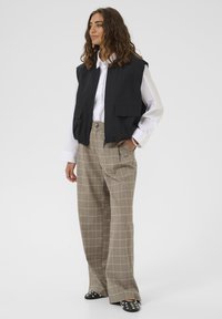 Fekete ujjatlan mellény, két elülső zsebbel, fehér ing és szürke kockás nadrág felett viselve. A cipők fekete alapúak, ezüst szegecsekkel.