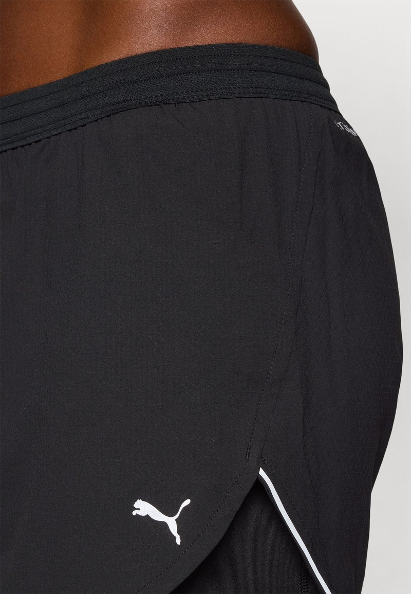 Pantaloni sportivi neri realizzati in tessuto leggero, con una superficie testurizzata, dettagli bianchi sui lati e un logo Puma bianco vicino all'orlo.