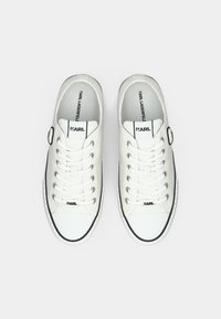 Een paar witte lage sneakers met zwarte accenten, veters en het "KARL LAGERFELD" logo op de tong en inlegzool, gezien van bovenaf.