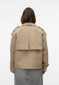 Manteau trench beige avec un design à revers, des boutons d'épaule et une coupe décontractée, associé à une jupe grise pour créer un contraste.