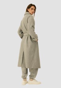 Jasnoszary wełniany długi płaszcz z szerokim kołnierzem, z paskiem w talii i bocznymi rozcięciami, w zestawieniu z dopasowanymi szarymi dresami i białymi sneakersami.