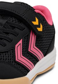 Chaussure de sport noire avec des bandes en chevron roses, doublure intérieure rose, lacets noirs, double flèche jaune sur la bride, et semelle blanche avec dessous beige.