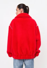 Jachetă oversized din blană artificială roșie, cu guler înalt, manșete cu textură ribbed și talie elastică. Textură netedă și detalii cu fermoar pe laterale.