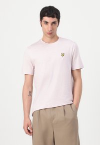 T-shirt à col rond de couleur rose clair, en mélange de coton, avec un petit logo de papillon jaune sur la poitrine gauche. Manches courtes, coupe décontractée.