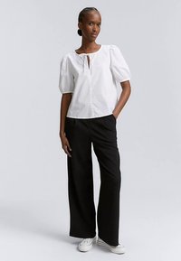 Bluza albă cu mâneci bufante și o deschidere tip cheie, asortată cu pantaloni negri largi și pantofi sport albi. Material neted, croială clasică.