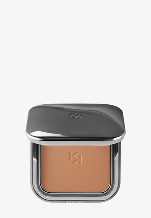 Poudre compacte dans un écrin argenté lisse et réfléchissant. Présente une poudre brun clair et lisse avec un logo embossé. Bords arrondis.