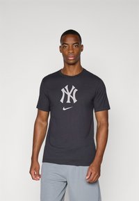 Black cotton t-shirt featuring a large grey NY logo and a small Nike logo. Crew neck, short sleeves, and a standard fit.