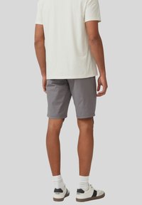Shorts en coton gris avec une coupe plate, des poches latérales et une coupe décontractée, associés à une chemise à manches courtes de couleur claire et des baskets blanches.