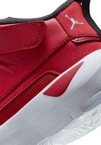 Sneaker rossa con una parte superiore in pelle liscia, accenti in rete, rifiniture nere e una suola in gomma bianca testurizzata con un design distintivo.