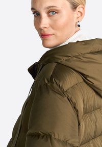 Doudoune verte olive avec capuche, présentant un léger brillant, une texture matelassée et un devant zippé. Couche blanche à col haut visible en dessous.