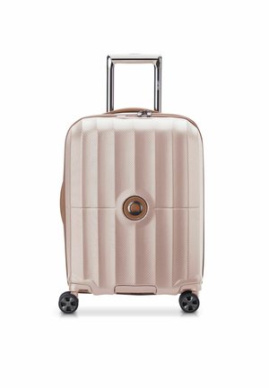 Hard-shell suitcase in pale pink with a textured finish, featuring a circular logo, retractable handle, and four black wheels.