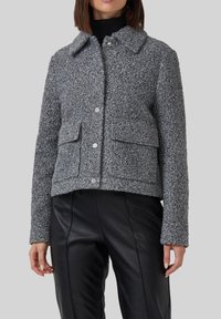 Giacca grigia con texture, colletto, bottoni a pressione e due tasche anteriori, abbinata a pantaloni in similpelle neri.