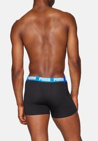 Schwarze Boxer-Shorts mit einem elastischen Bund und blauem Puma-Logo. Der Stoff ist glatt und schmiegt sich eng an, zeigt ein schlichtes Design ohne Muster.