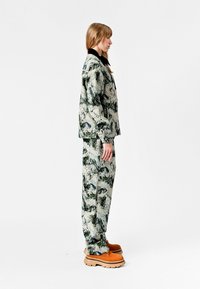 Conjunto de dos piezas con estampado que incluye una chaqueta ligera y texturizada y pantalones a juego en tonos grises y verdes, complementado con zapatos marrones.