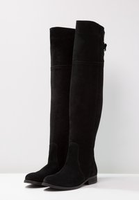 Botas negras de ante por encima de la rodilla con suela plana, puntera redonda y detalles de costura sutiles. Textura suave, sin hardware o acentos visibles.