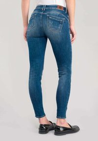 Jeans in denim blu slim con vita media, tasche posteriori e leggera scoloritura. Indossati con ballerine nere, mostrano una silhouette aderente.