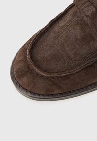 Καφέ σουέντ παπούτσι για να το φοράτε εύκολα, με στρογγυλεμένη μύτη και αντίθετη ραφή κατά μήκος της σόλας, με υφή και διακριτικές λεπτομέρειες σχεδίασης.