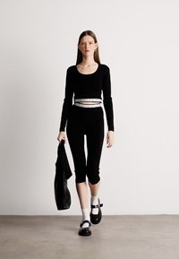 Μαύρη μπλούζα με μακριά μανίκια και στρογγυλή λαιμόκοψη, συνδυασμένη με μαύρο κοντό κολάν. Το μοντέλο έχει προσθέσει αξεσουάρ με μια μαύρη τσάντα και μαύρες πλατφόρμες.