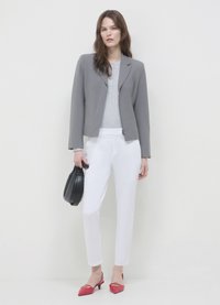 Grauer Blazer über einem hellgrauen Oberteil, kombiniert mit weißen Hosen. Abgerundet mit roten spitzen Absatzschuhen und einer schwarzen Handtasche.