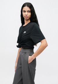 Fekete rövid ujjú póló, amelynek derékrészén csomó van, fehér Nike logóval. Magas derekú, szürke, bő szárú nadrággal párosítva.